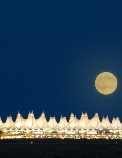 A full moon rising behind a lit, tent-like structure at twilight.