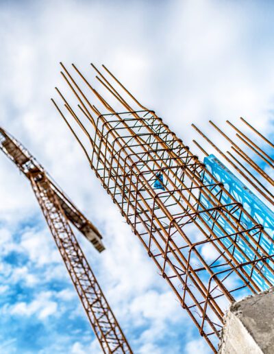 Construction site with rebar structure and crane under a blue sky with clouds.