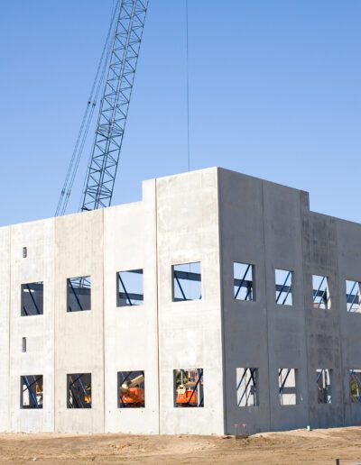 Erection of prefabricated concrete walls at a construction site with a crane in the background.